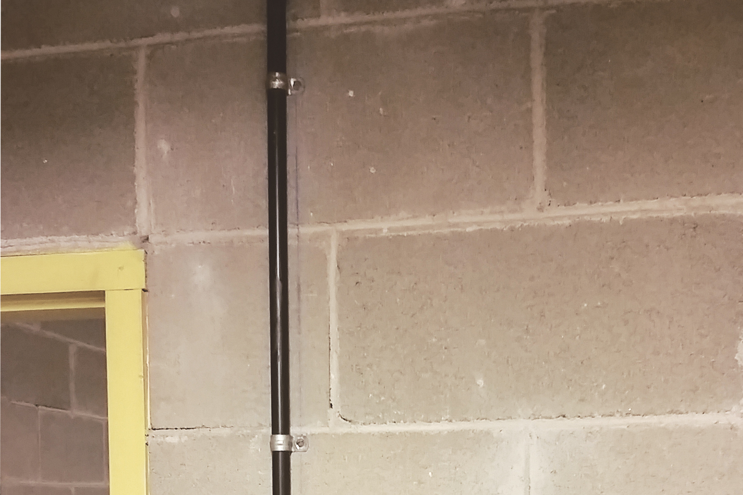 Imagen de aplicación del clip de fijación FT: Fijación de un tubo metálico a la pared de hormigón de una obra en construcción
