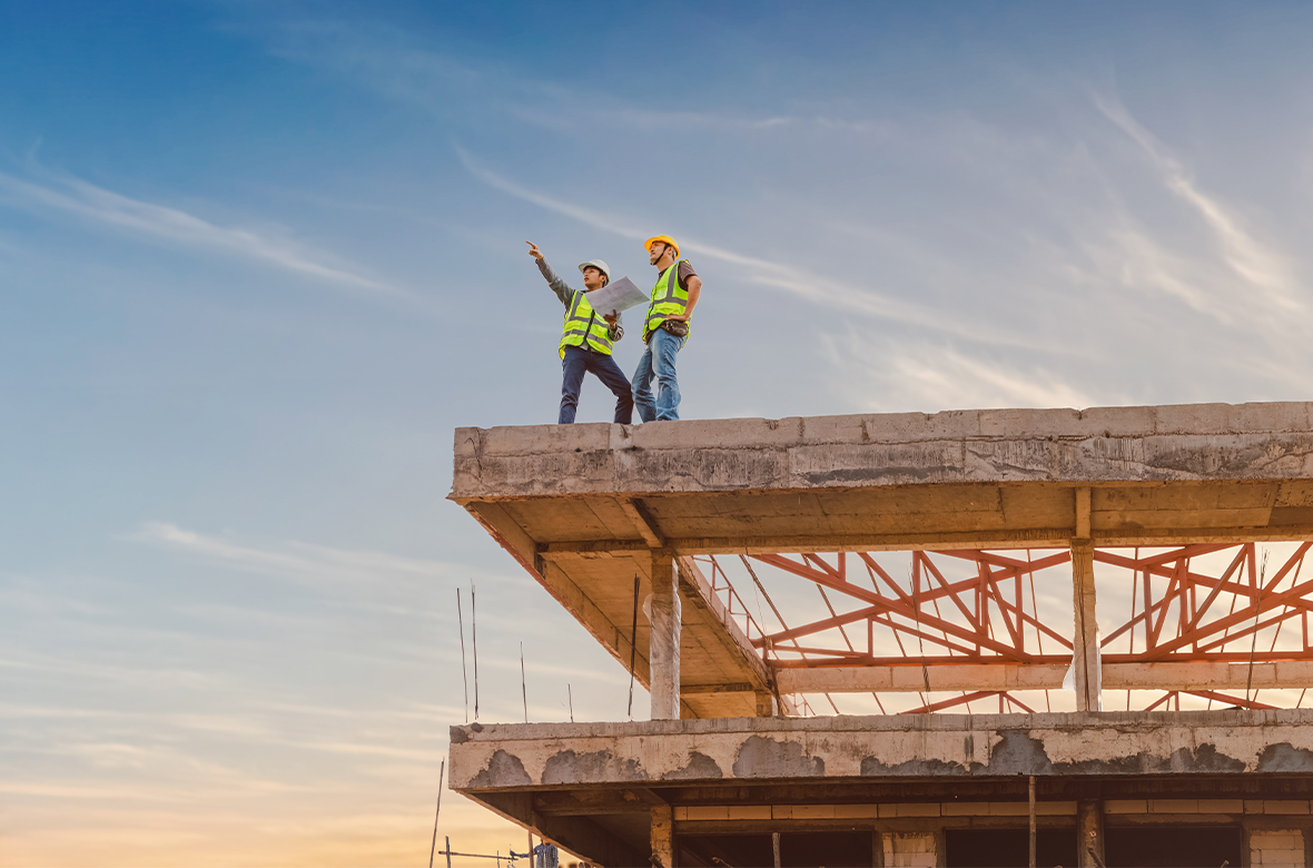 Dos trabajadores encima de una obra de construcción, apuntando al cielo