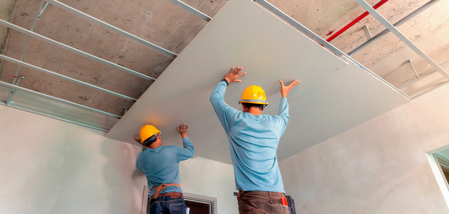 Instaladores fijando una placa de pladur en una estructura para falso techo