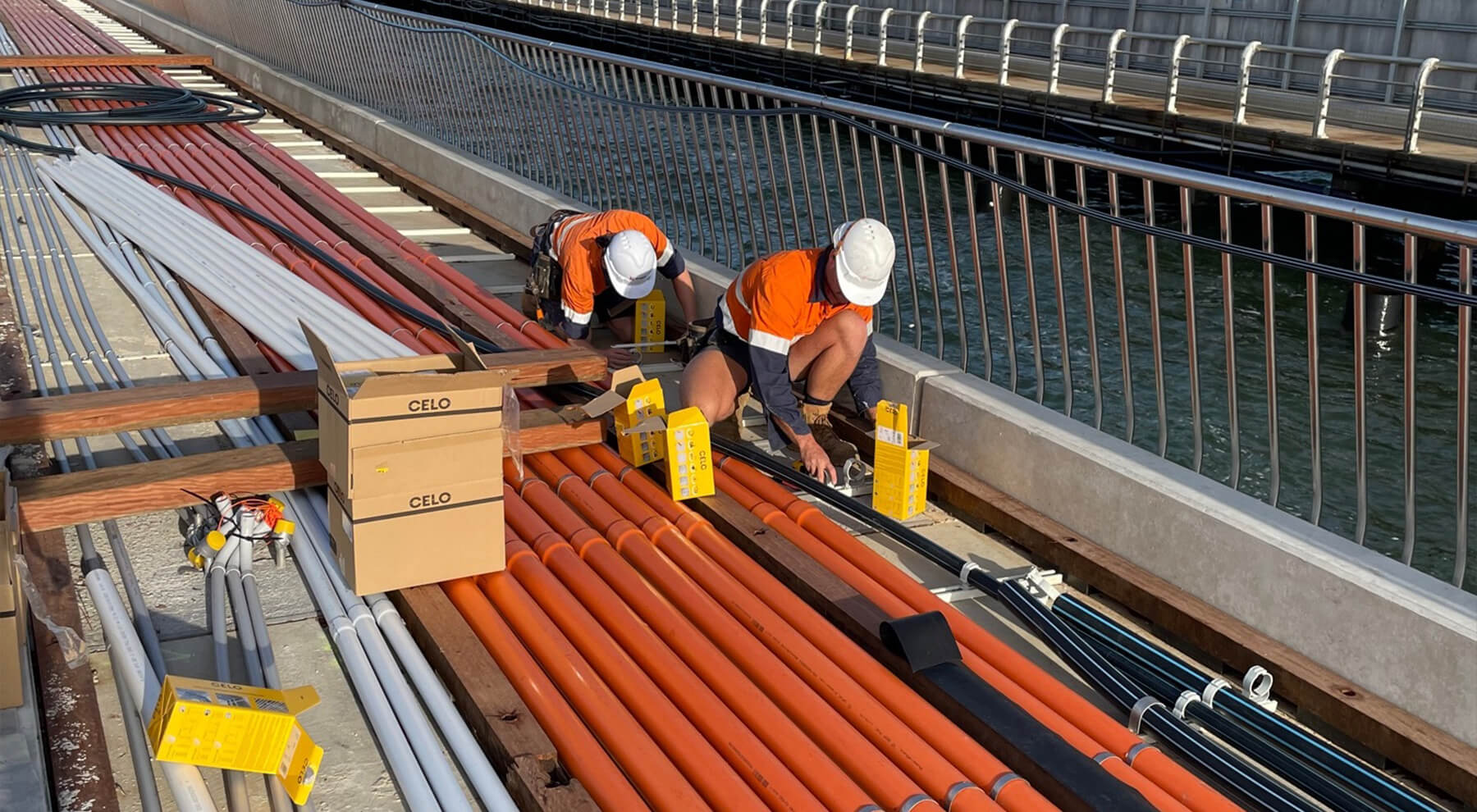 Dos instaladores en el puernte de Melbourne instalando abrazaderas metálicas de CELO para la sujeción de tuberías