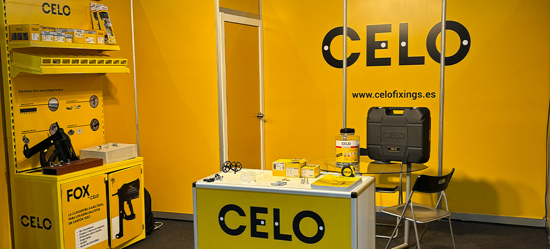 Stand de CELO en la feria ADIP con mostrador amarillo con una pistola de clavos FOX y otros productos