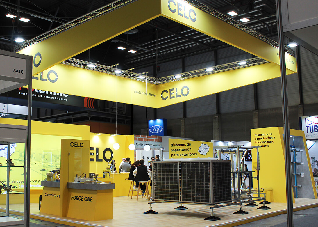 Stand de CELO en la feria C&R con estructura y mostradores amarillos y expositores de productos de fijación y suportación