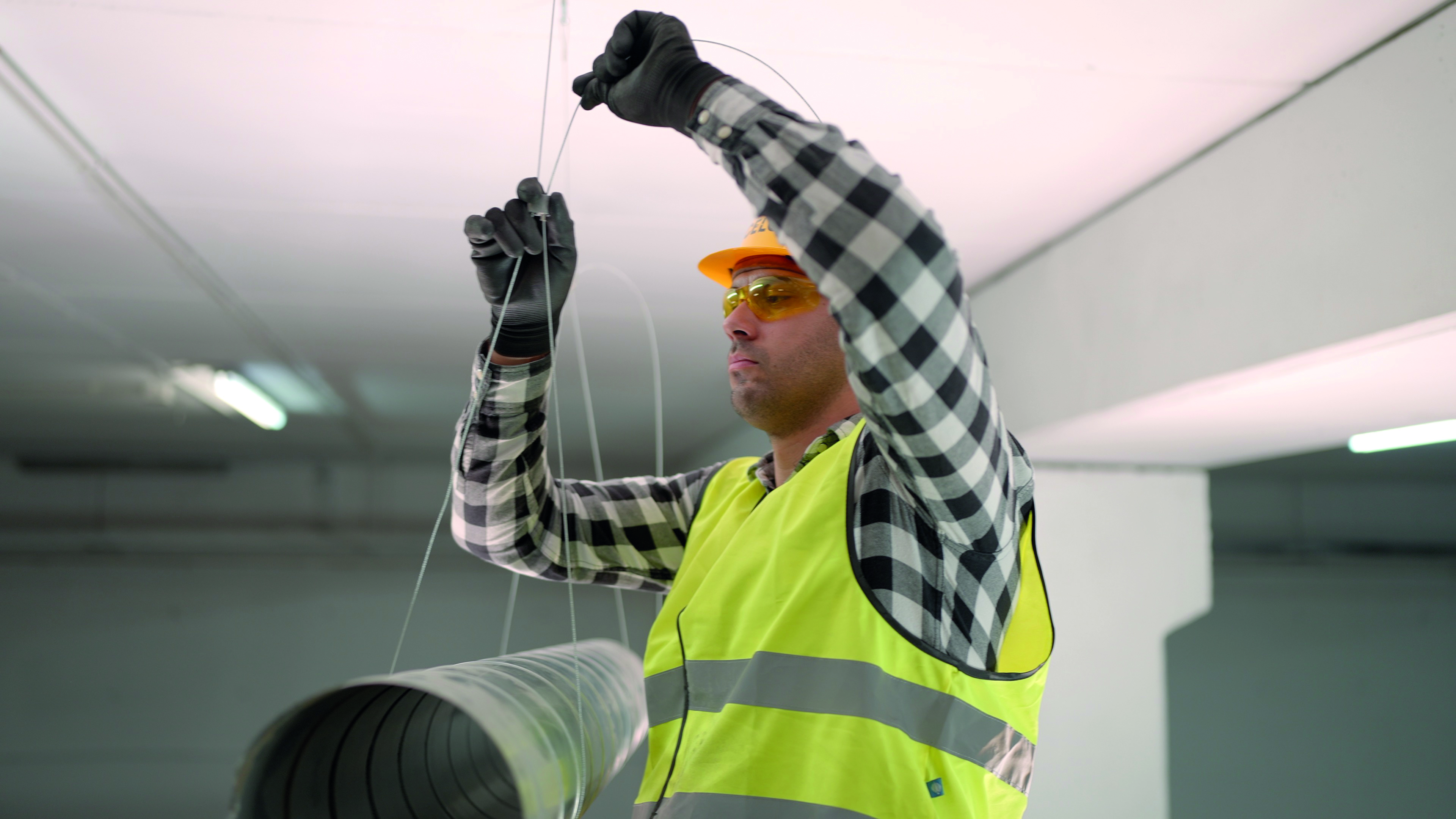 Técnico instalando cables de suspensión como parte de un sistema suspensión de cables en una estructura interior