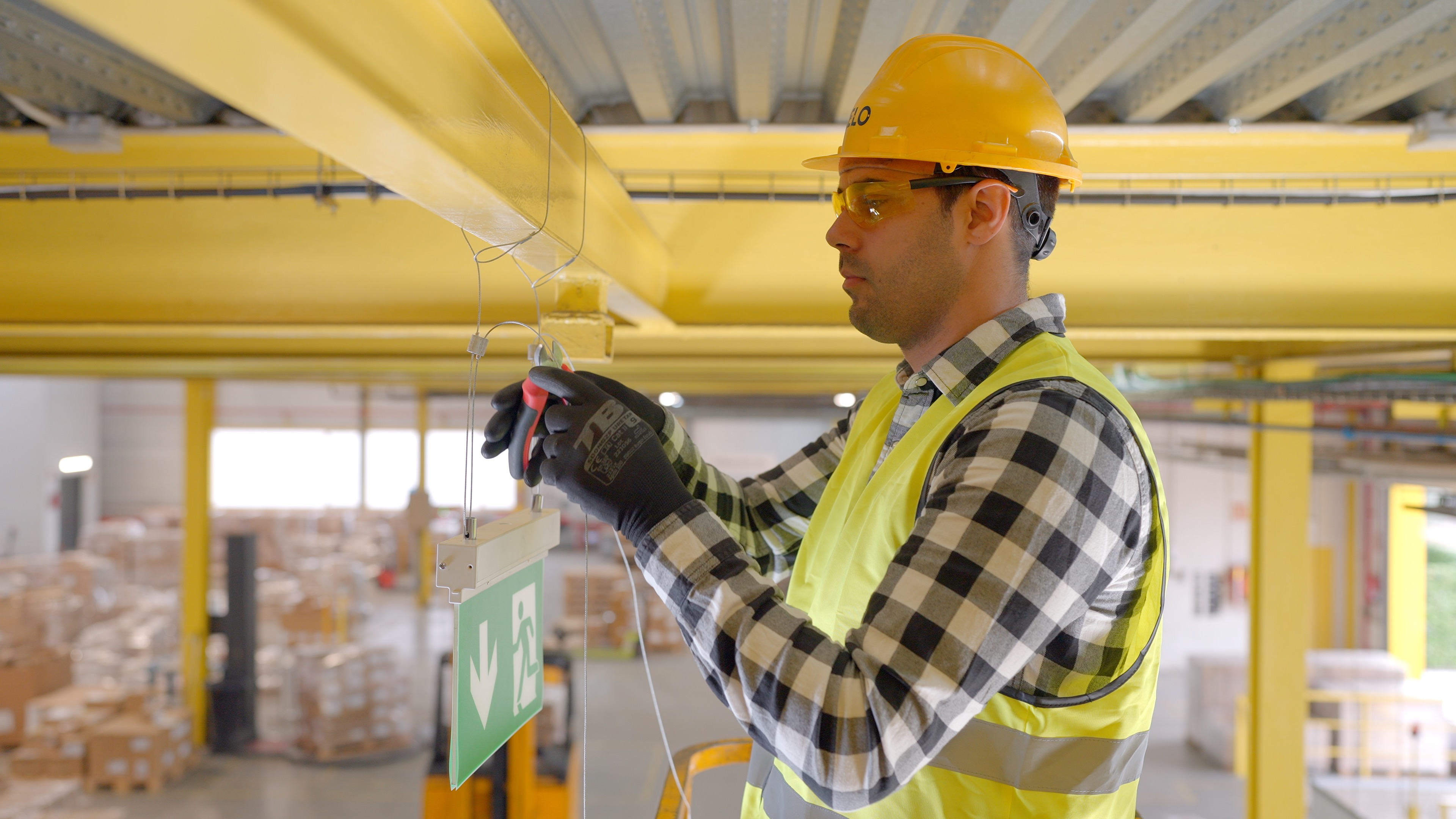 Trabajador instalando cables de suspensión como parte de un sistema suspensión de cables para colgar señalización en una nave industrial